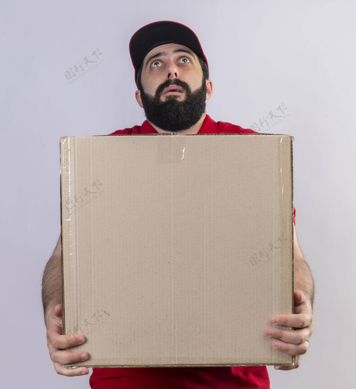 向上印象深刻的年轻英俊的白人送货员穿着红色制服 戴着帽子拿着纸箱 抬头望着孤立的白色制服帅气交货