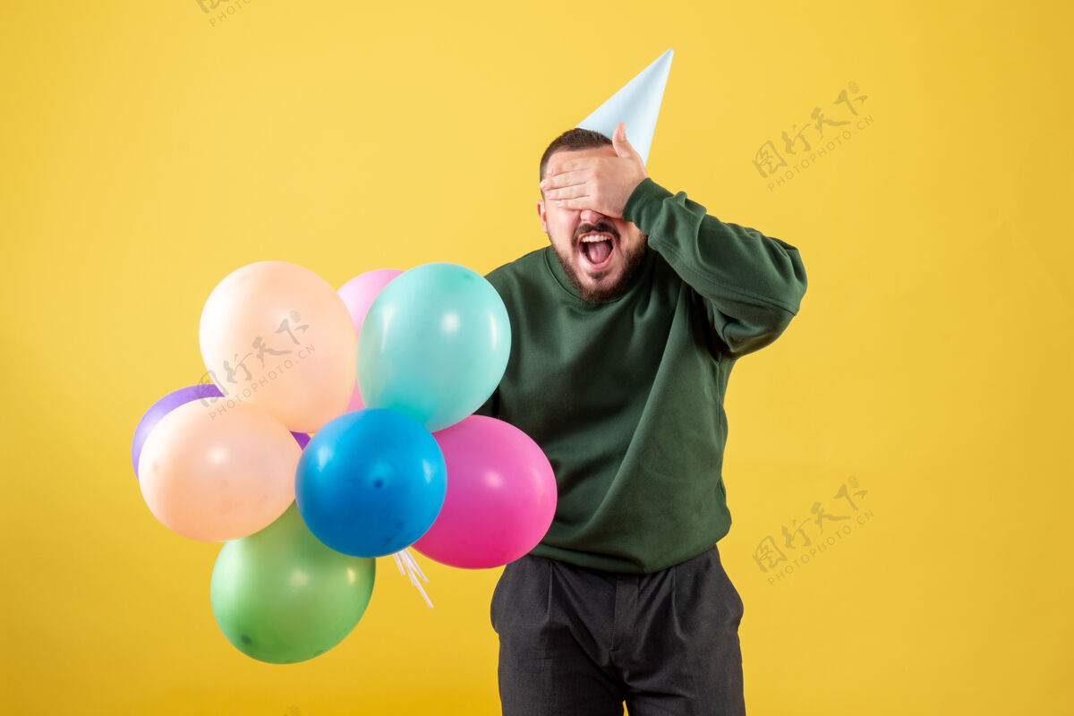 年正面图黄色背景上有彩色气球的年轻男性欢乐庆祝购物