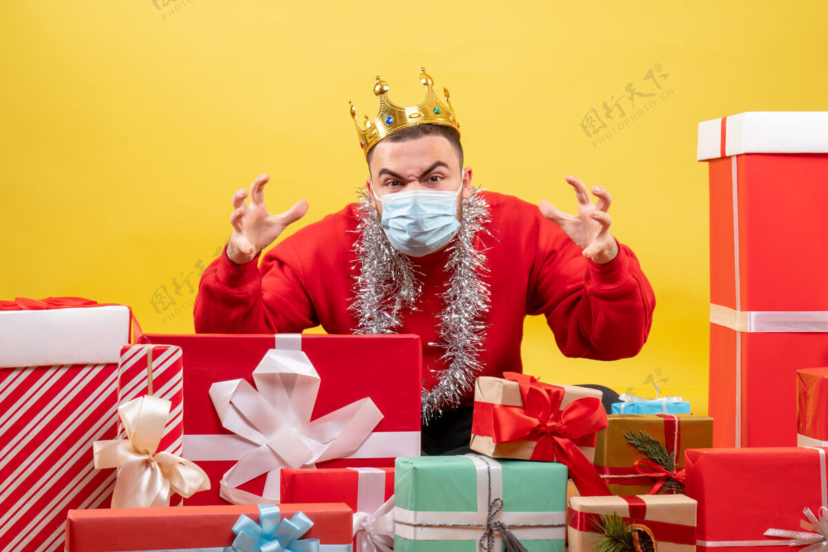 圣诞节正面图：坐在圣诞节周围的年轻男性戴着黄色背景的面具出现成人礼物礼物