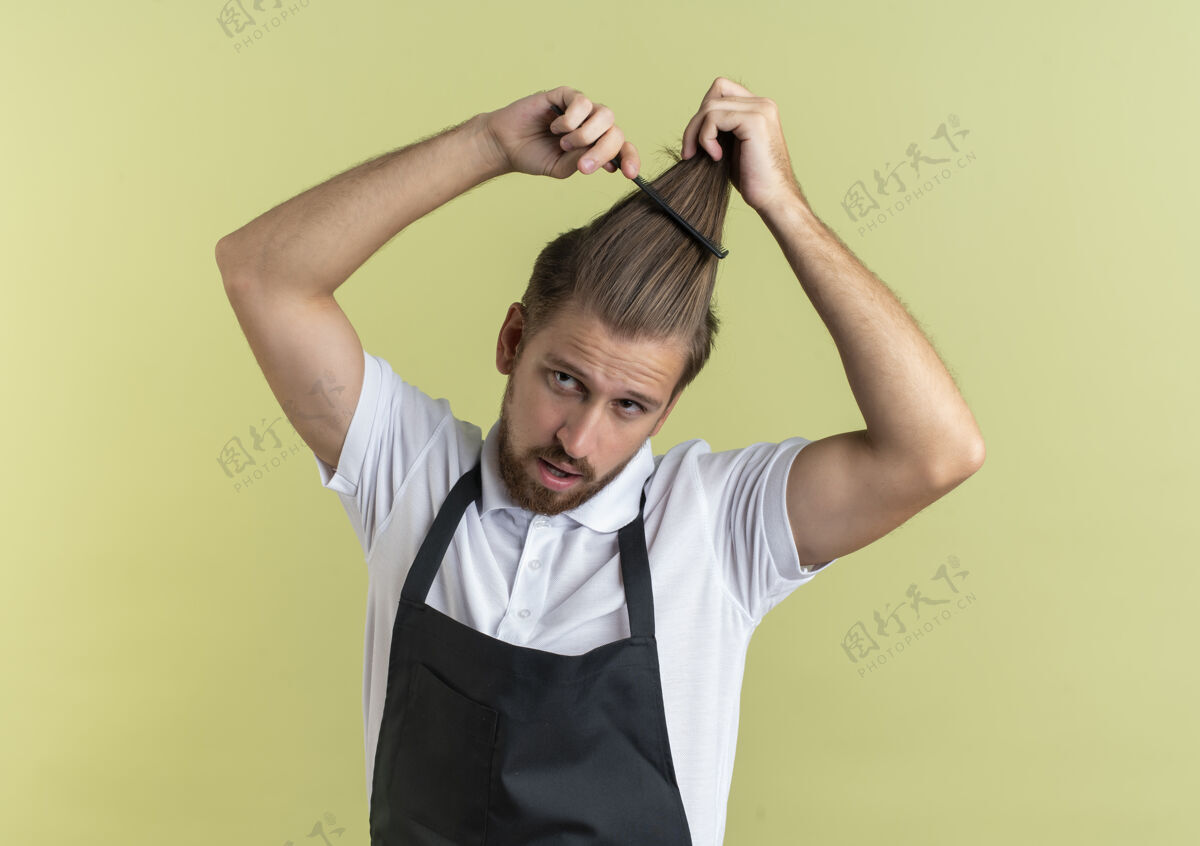 年轻自信的年轻英俊的理发师梳着头发 望着橄榄绿上孤零零的一面帅气理发师头发