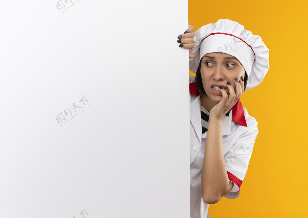 壁板焦急的年轻女厨师身着厨师制服 站在白色的墙后 手放在脸颊上 看着旁边的橘色空间站橙色焦虑
