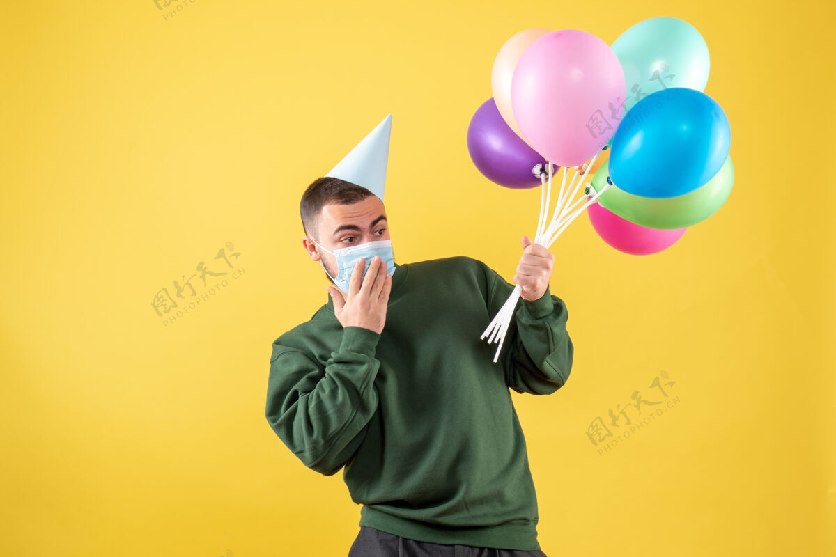 生日正面图年轻男子手持五颜六色的气球站在黄色的聚会年快乐