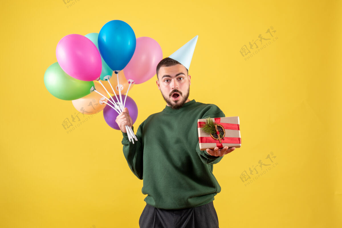 背景正面图：手持彩色气球的年轻男性 呈现在黄色背景上聚会礼物年轻男性