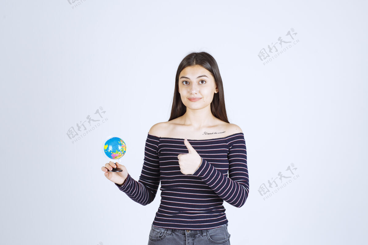想象力穿着条纹衬衫的年轻女子拿着一个迷你地球仪 看起来很兴奋世界女人女性