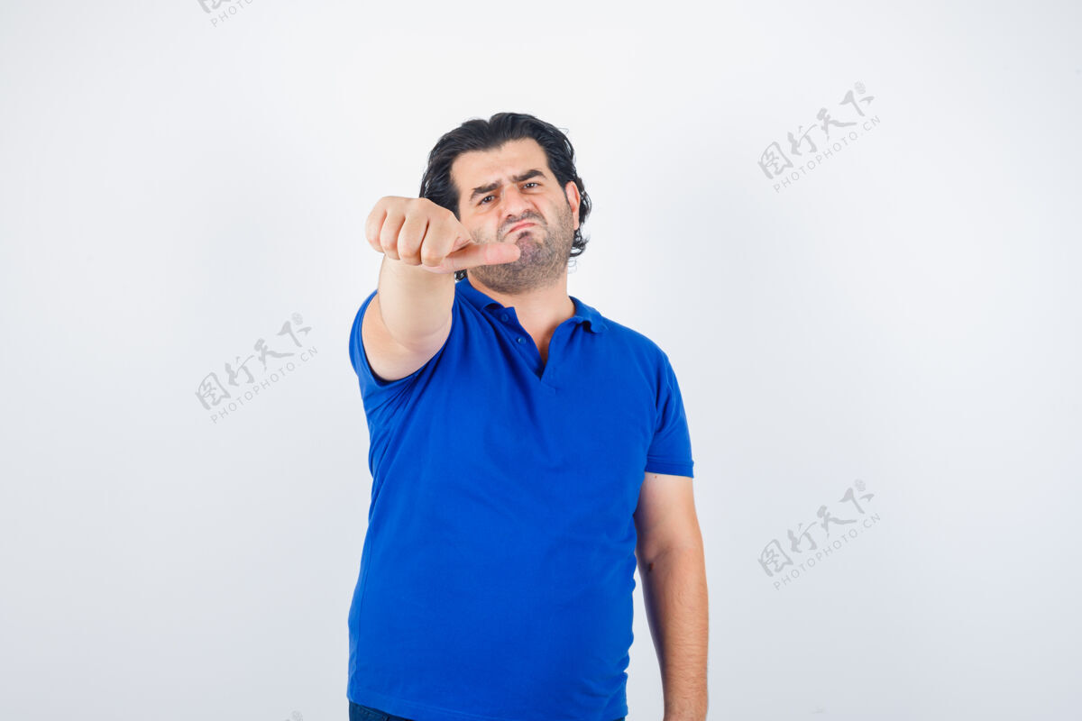 沮丧成熟的男人指着旁边的拇指在蓝色t恤 牛仔裤和失望的样子 前视图表情拇指牛仔裤