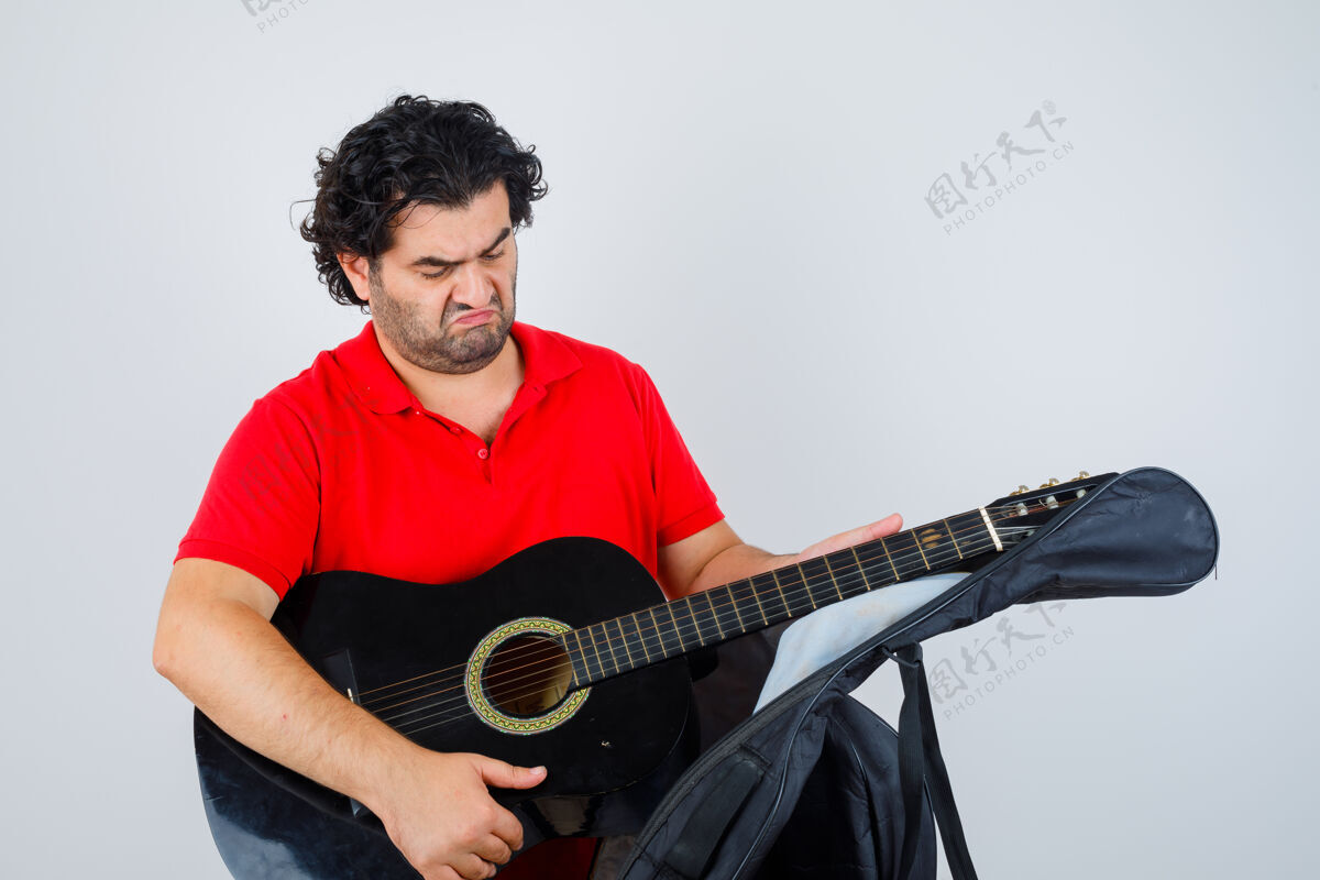 创意穿着红色t恤的帅哥从箱子里拿着吉他 神情沉思 正对着窗外吉他带案例