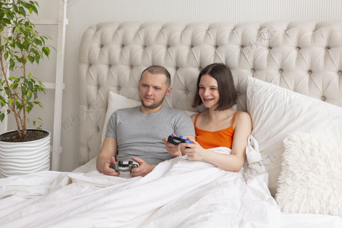 玩家夫妻俩在床上玩电子游戏享受操纵杆游戏