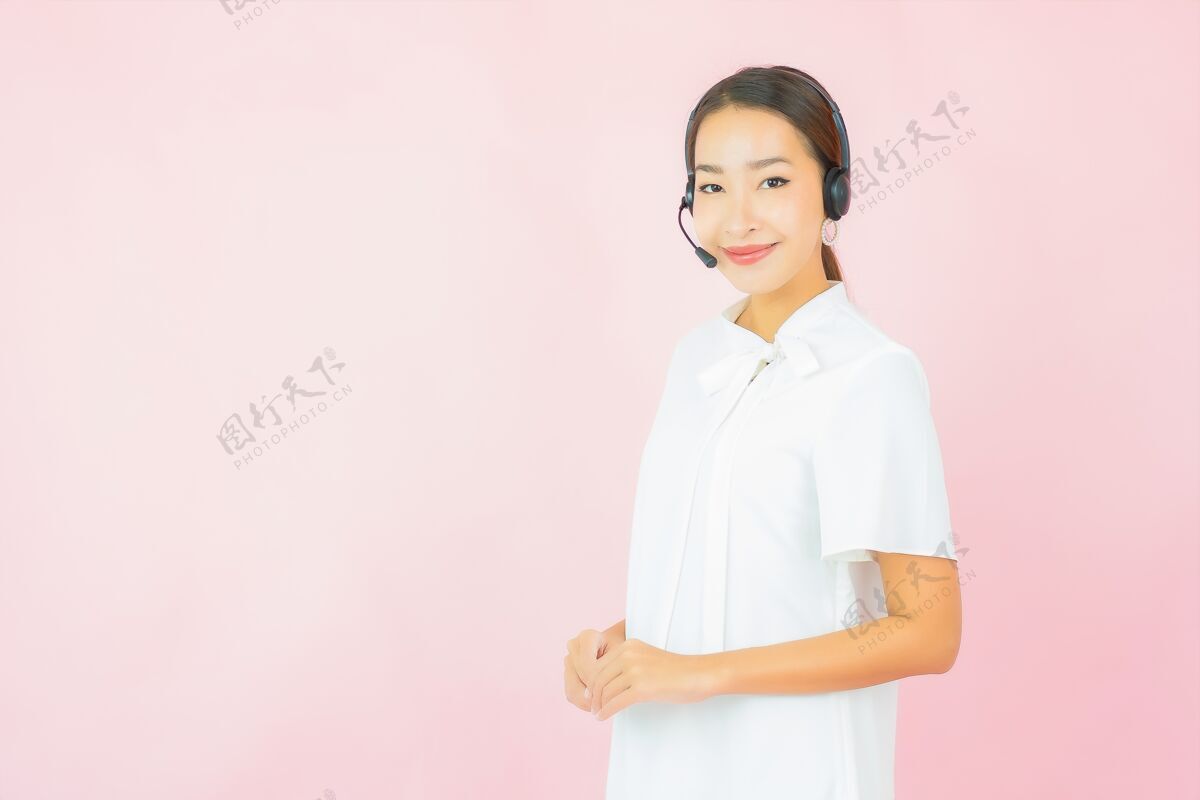 服务在粉色墙上为呼叫中心客户描绘一位戴着耳机的美丽亚洲年轻女子人接线员肖像