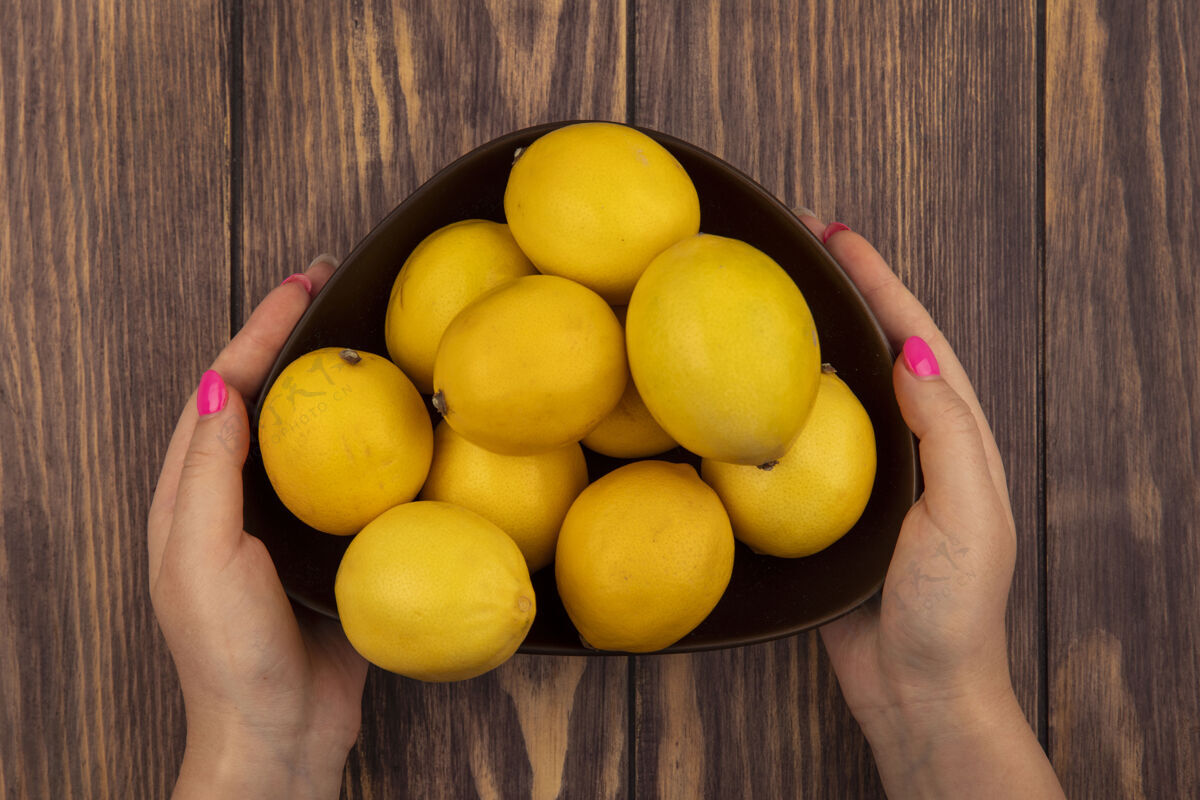 食物顶视图中的女性手拿着一碗新鲜的柠檬在木墙上女性持有柑橘