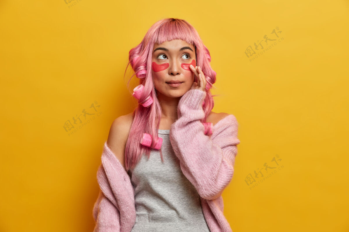 沉思严肃沉思的亚洲粉红头发女人 头上戴着卷发 抚摸着健康柔软的皮肤贴片亚洲人美容粉色