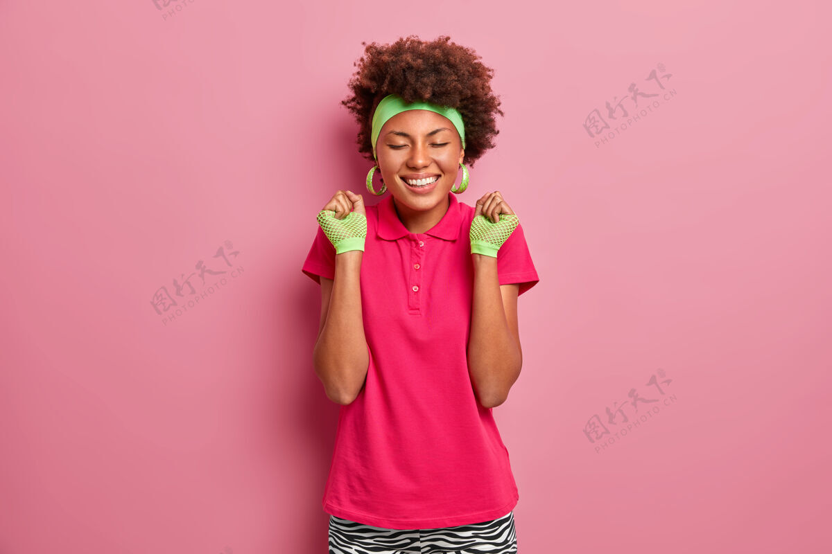 快乐快乐的情绪和感觉微笑的黑人女孩穿着粉色t恤 戴着运动手套和头带 高兴地握紧拳头 感受胜利的滋味 庆祝比赛胜利赢家高兴庆祝