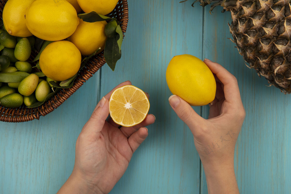 桶女性手拿新鲜柠檬和水果的俯视图 比如金盏花和柠檬放在蓝色木墙上的桶上视野厨房食物