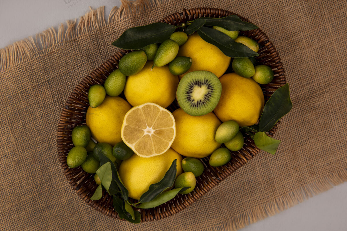 饮食顶视图新鲜水果 如猕猴桃金盏花和柠檬桶上的麻袋布上的灰色墙壁食物柠檬人