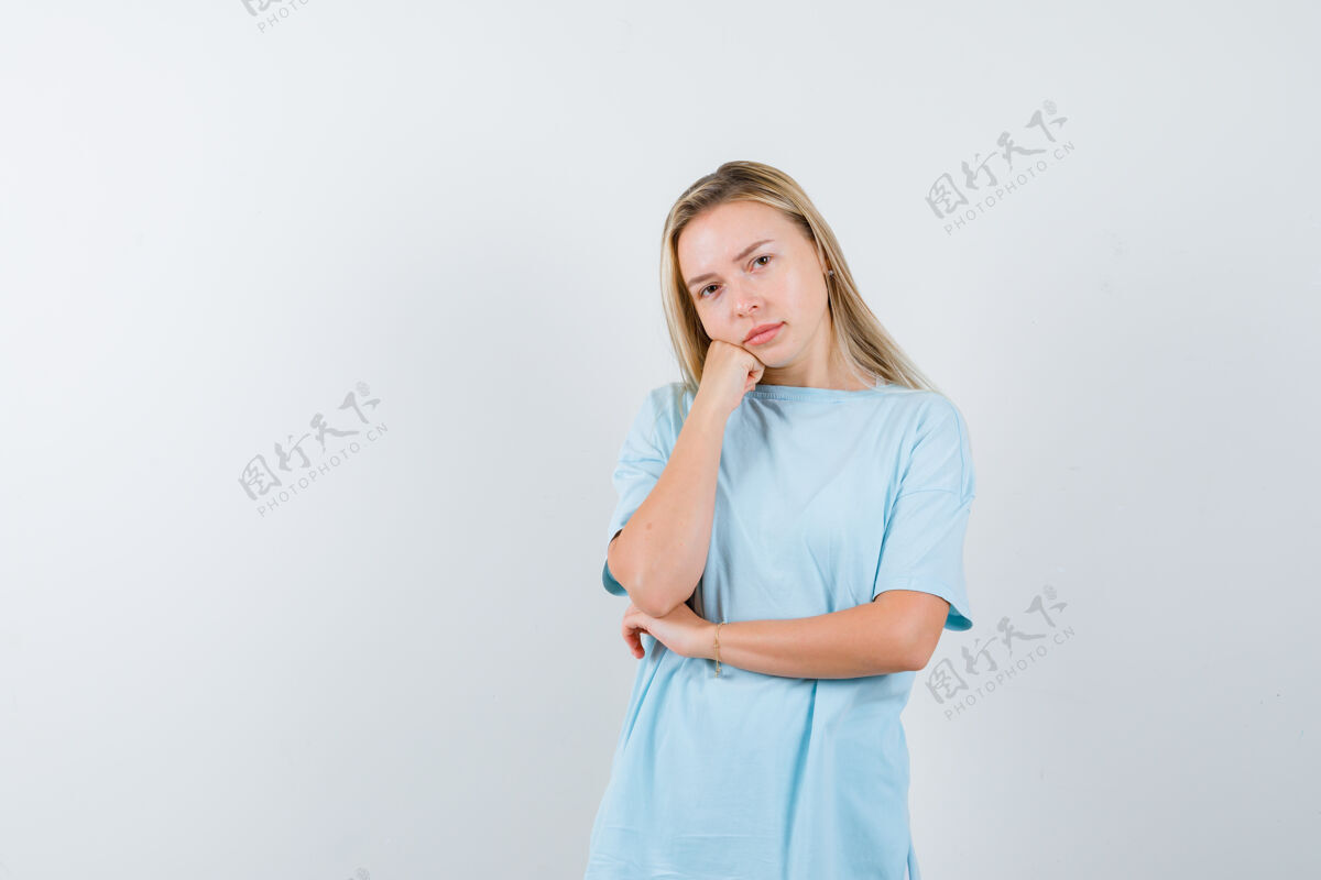 健康金发女孩靠在手掌上 站在思考的姿势在蓝色t恤衫 看起来沉思 前视图模特旅游漂亮