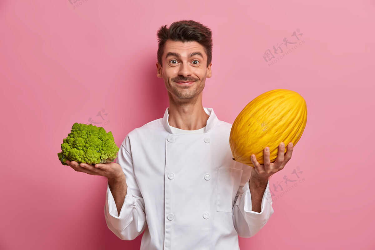 选择积极的欧洲男厨师准备沙拉 拿着大瓜和花椰菜高兴蔬菜粉色