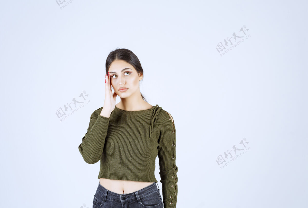 姿势一个穿着绿色上衣的年轻模特在想白墙上的东西人类模特女人