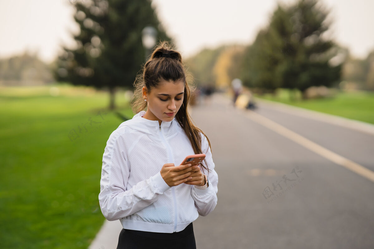 运动装年轻女运动员慢跑后手持并使用智能手机休闲街道成功
