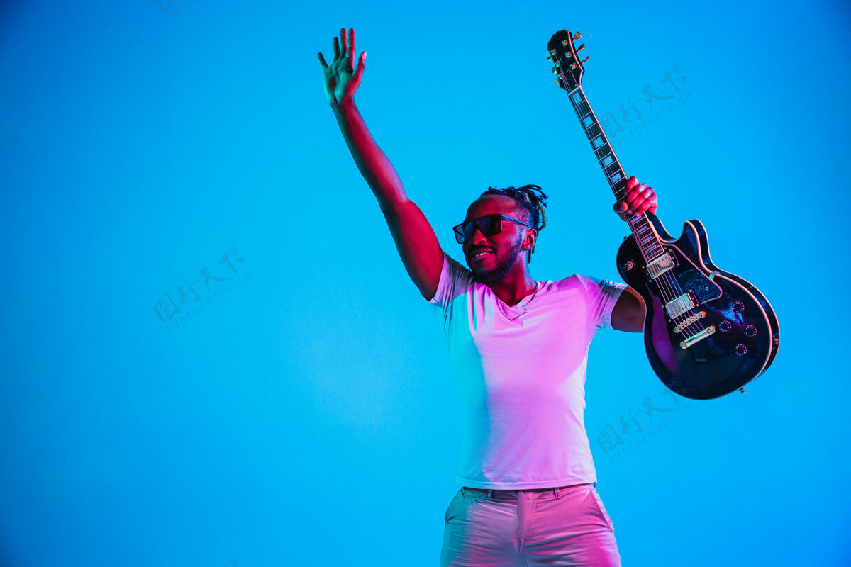 著名年轻的非洲裔美国音乐家在霓虹灯下像摇滚明星一样在蓝色背景下弹吉他复古音乐会单身