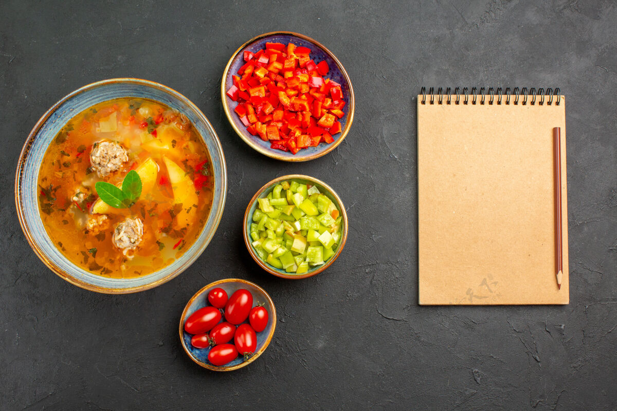笔记本在深色的餐桌上俯瞰美味的肉汤和辣椒片 菜品照片美食盘子碗食物