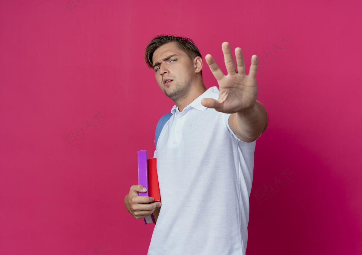 穿年轻帅气的男学生背着书包 伸出手孤立在粉红色的墙上帅气年轻姿态