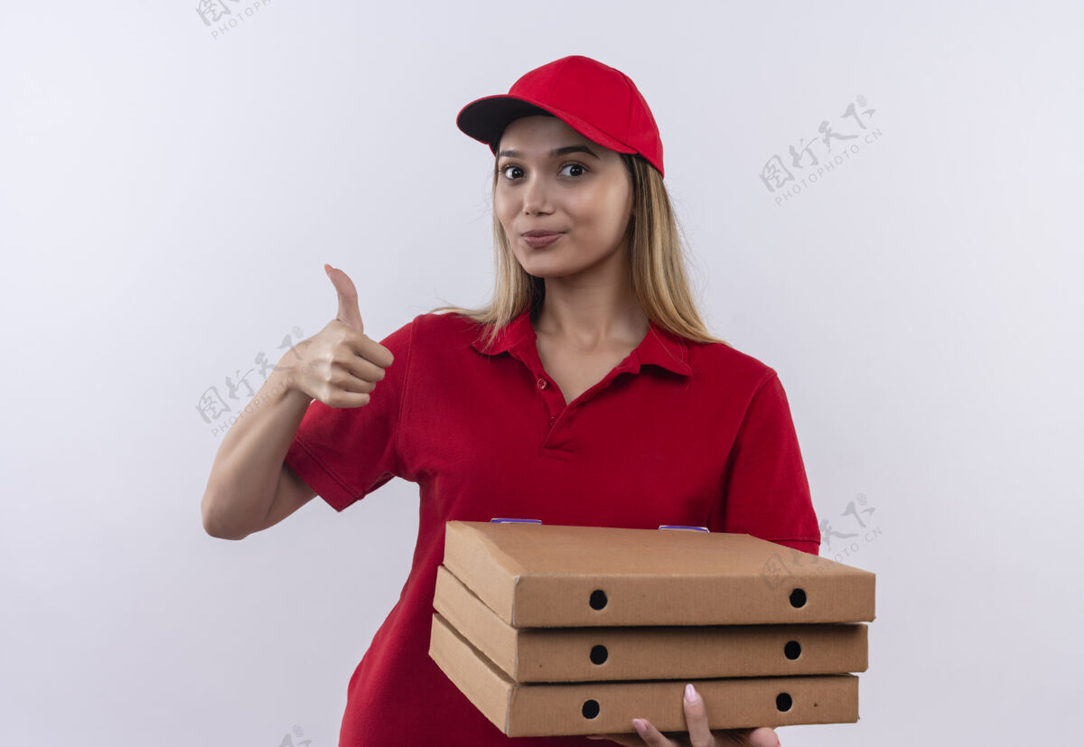 年轻人穿着红色制服 头戴鸭舌帽 拿着披萨盒的年轻送货女孩高兴地把大拇指孤立地竖在白色的墙上拇指请穿送货