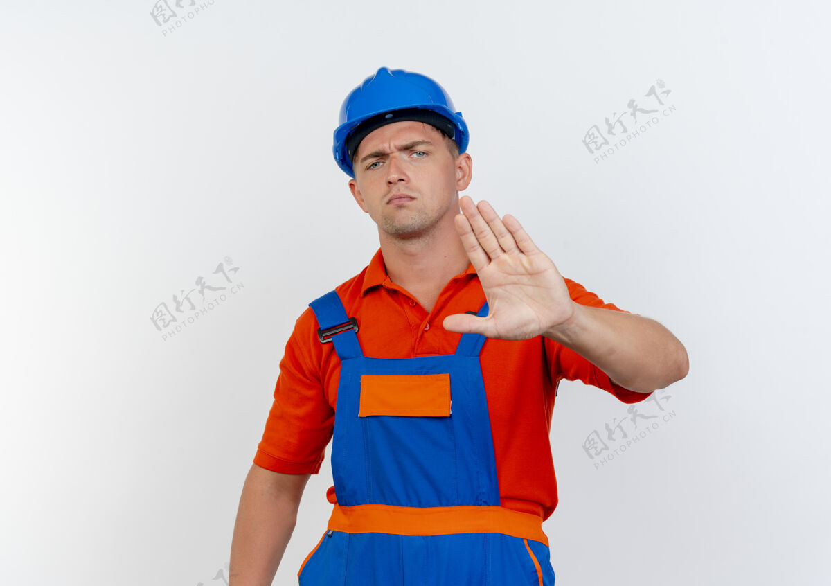年轻严格的年轻男性建筑工人穿着制服 戴着安全帽 在白色地板上做停车手势男性白色手势