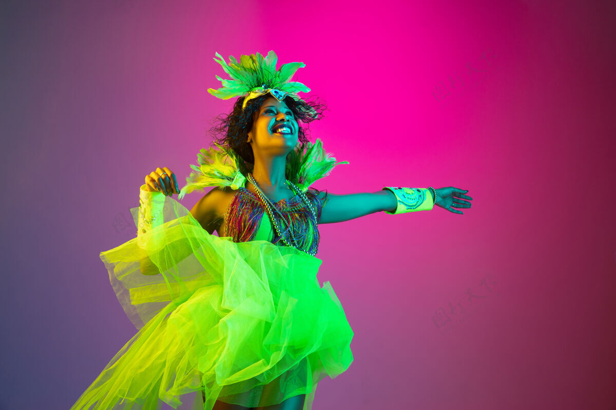 人类美丽的年轻女子在嘉年华 时尚的化装服装与羽毛跳舞的梯度背景在霓虹灯下黄金聚会化妆舞会