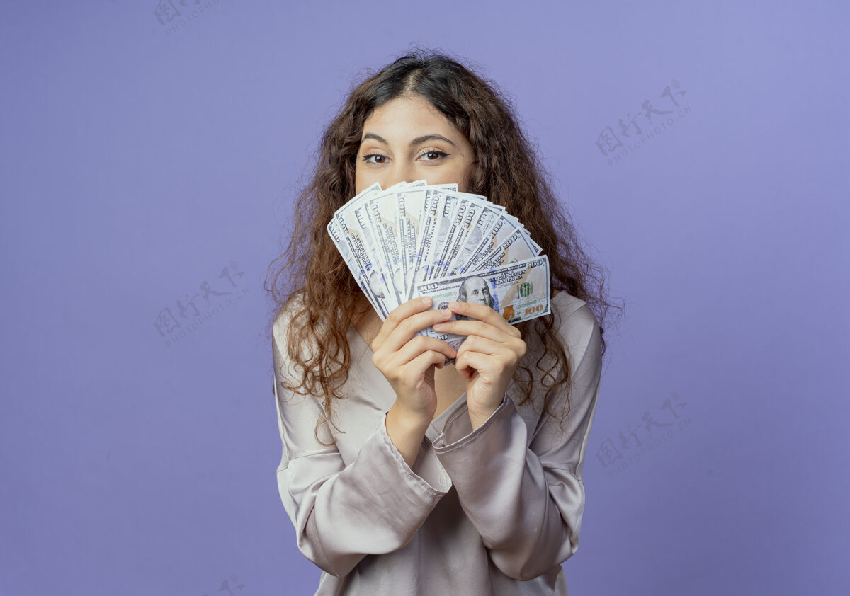 年轻年轻漂亮的女孩脸上贴满了钱隔离在蓝色的墙上钱掩护漂亮