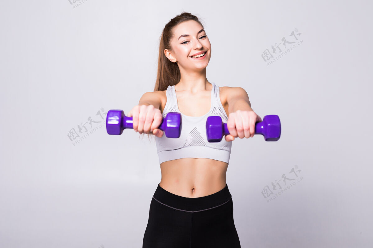 力量健康的女人 带着哑铃在白墙上锻炼健身馆的概念设备欢呼强壮