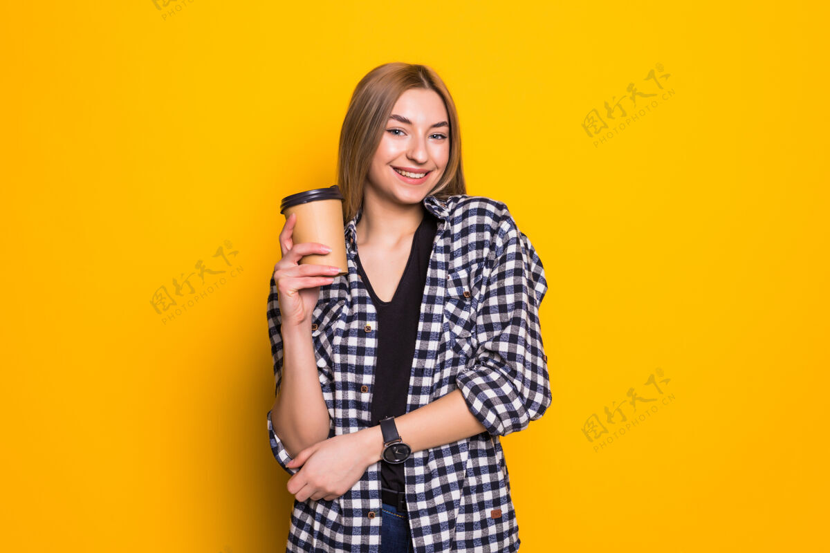 纸我最喜欢的饮料穿着休闲服的可爱的年轻女子 手拿咖啡杯 越过黄色的墙壁姿势漂亮美丽