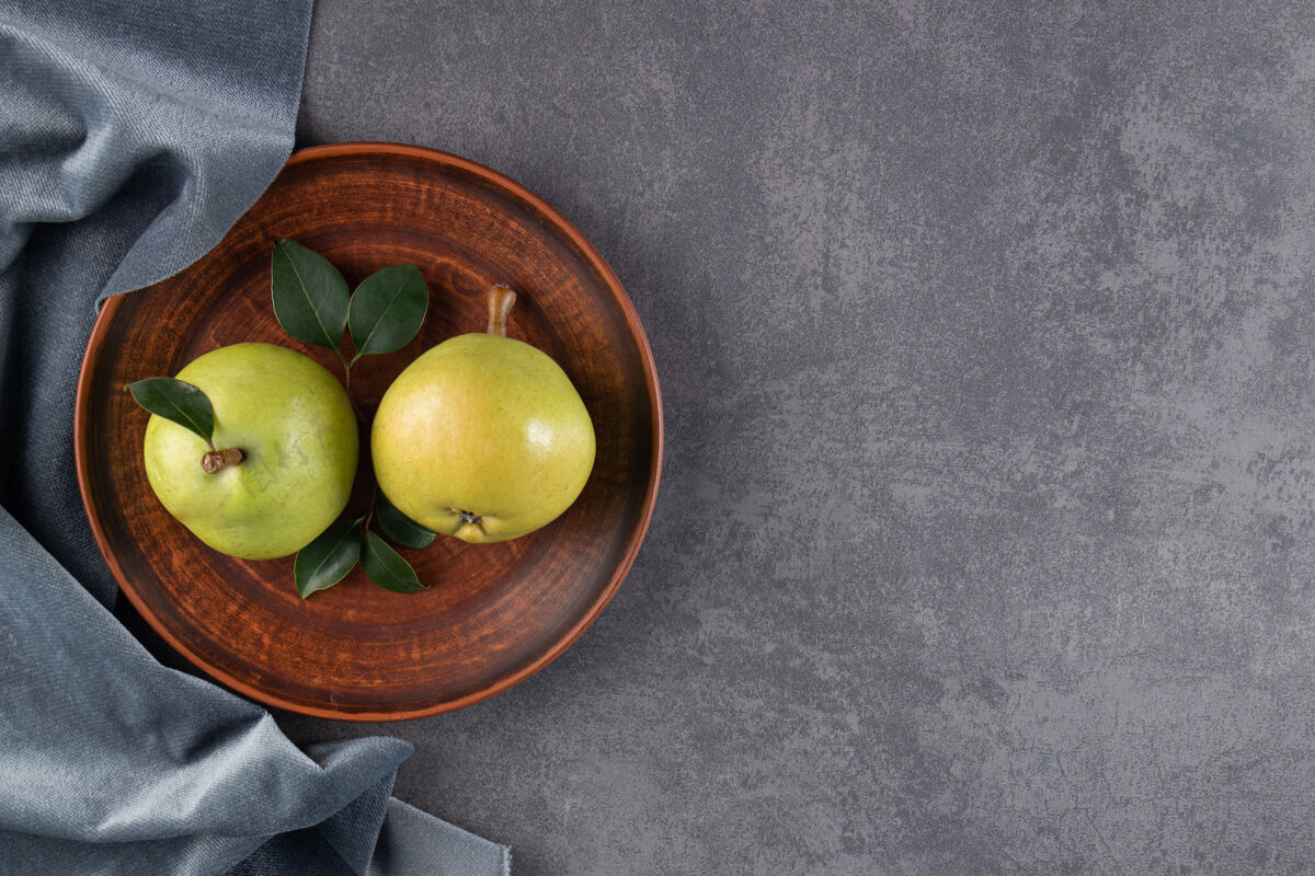 生的两个熟透的梨子放在一个盘子和一块布上 放在蓝色的桌子上美味梨多汁