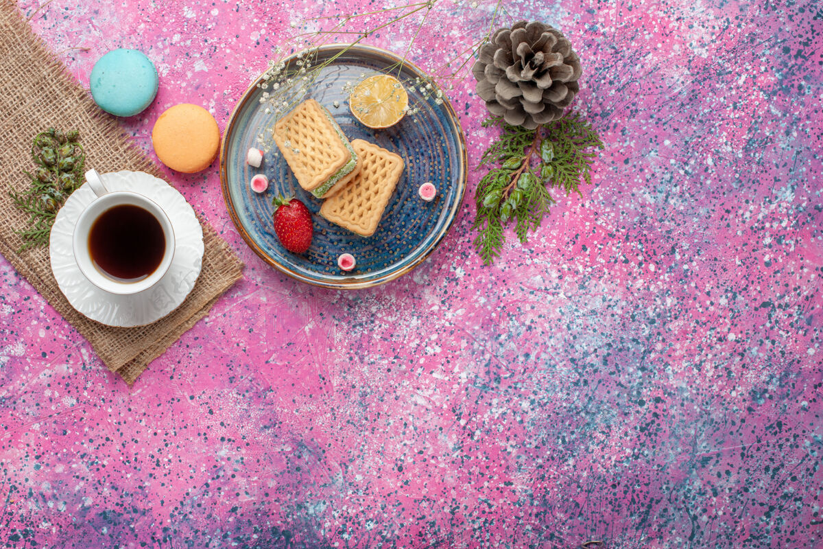五颜六色俯瞰美味的华夫饼 在粉红色的表面上放上一杯茶和麦卡龙鲜花茶华夫饼