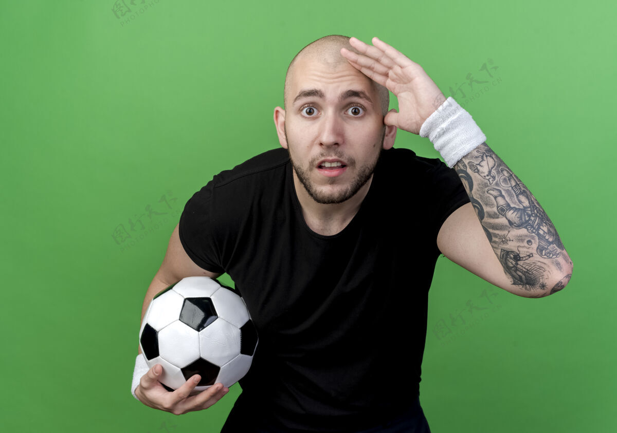 年轻惊讶的年轻人戴着腕带拿着球 看着远处的绿色隔离手距离球手