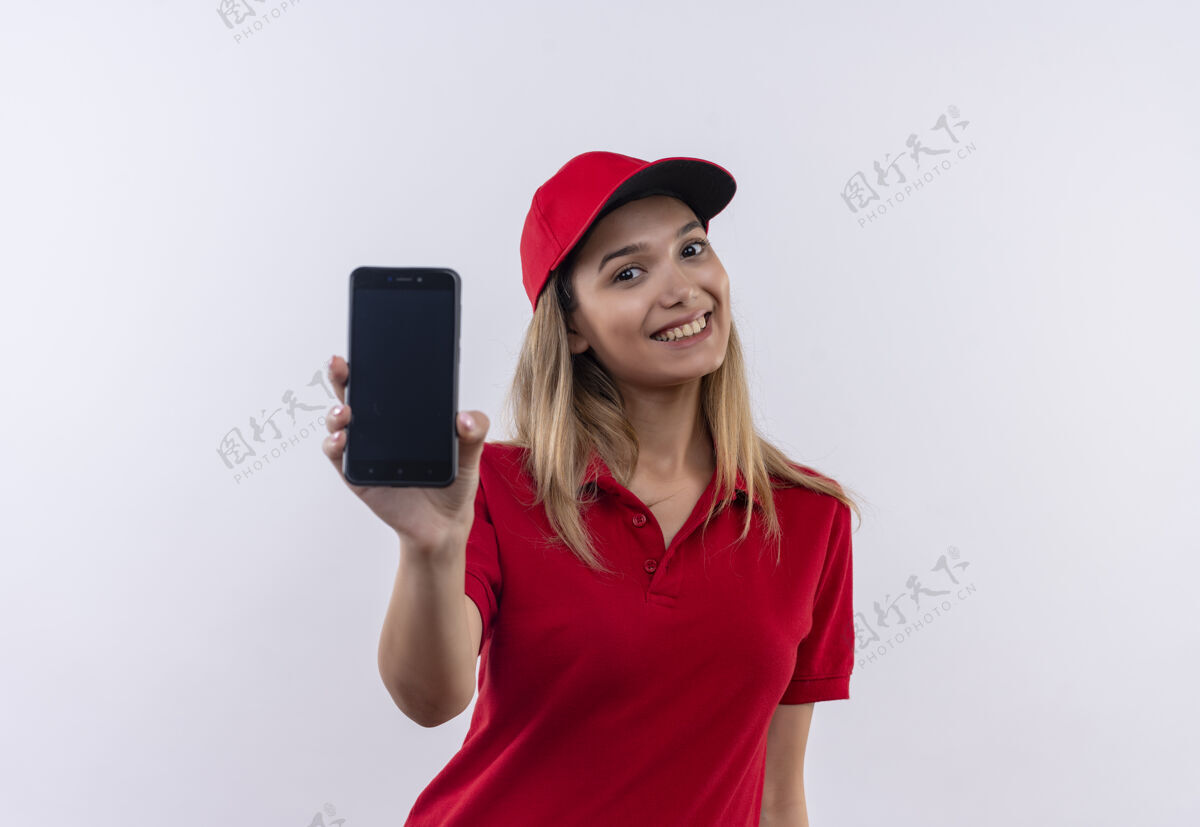 手势面带微笑的年轻送货女孩身穿红色制服 戴着帽子 手持手机对着隔离在白色上的相机表情女人帽子