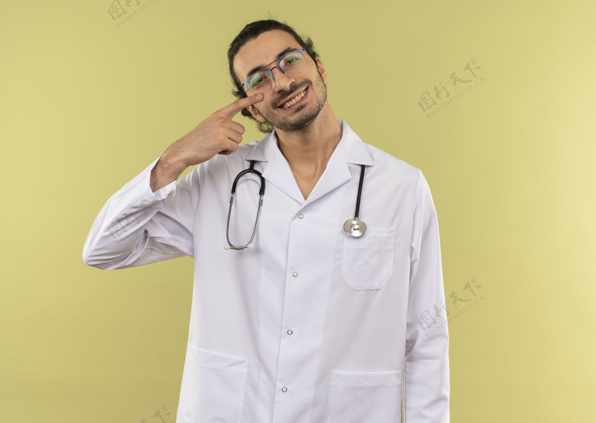 光学年轻的男医生面带微笑 戴着眼镜 身穿白色长袍 手持听诊器 眼睛盯着绿色微笑眼睛白色