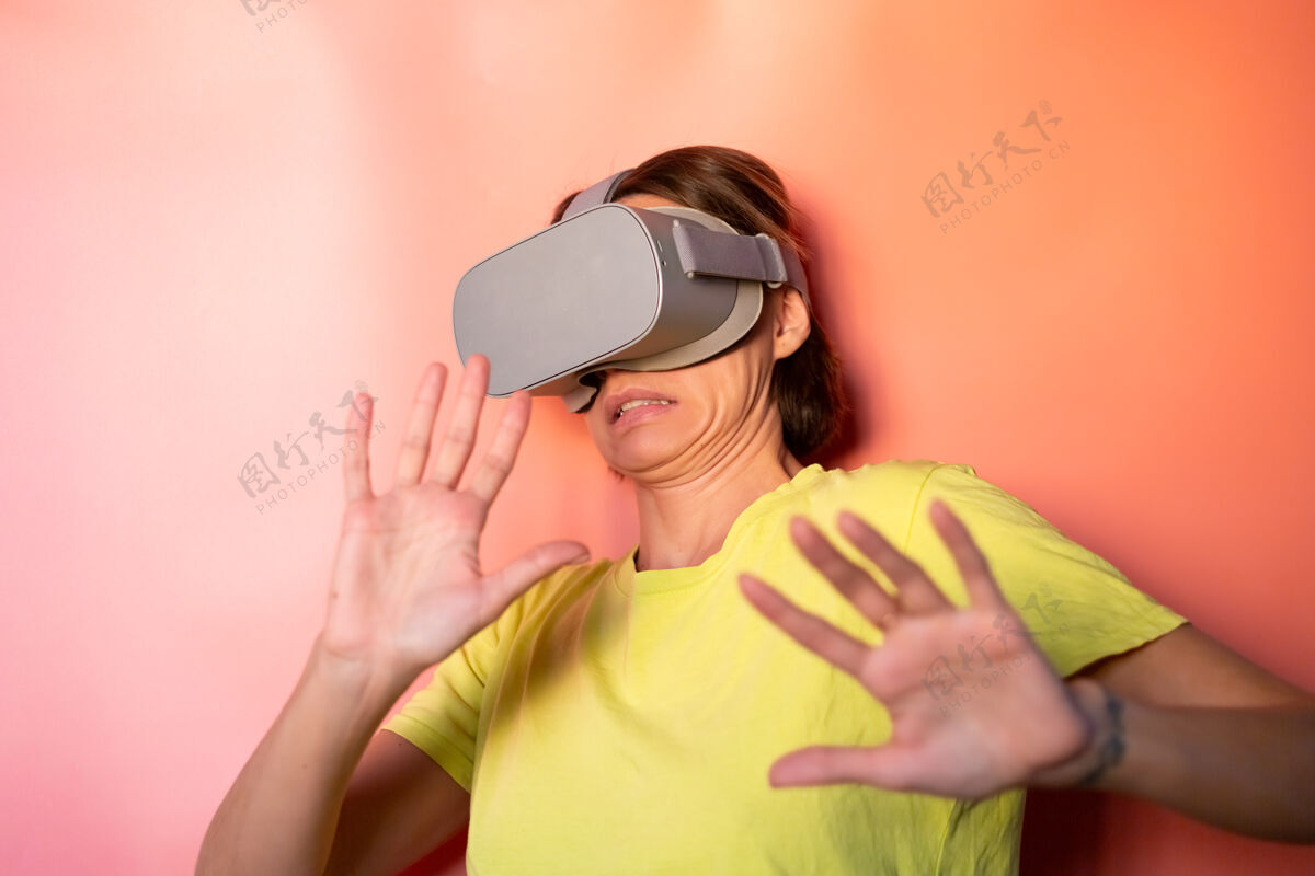 智能在粉红色橙色背景的工作室里 戴着虚拟现实眼镜的女人的情感肖像手势女性娱乐