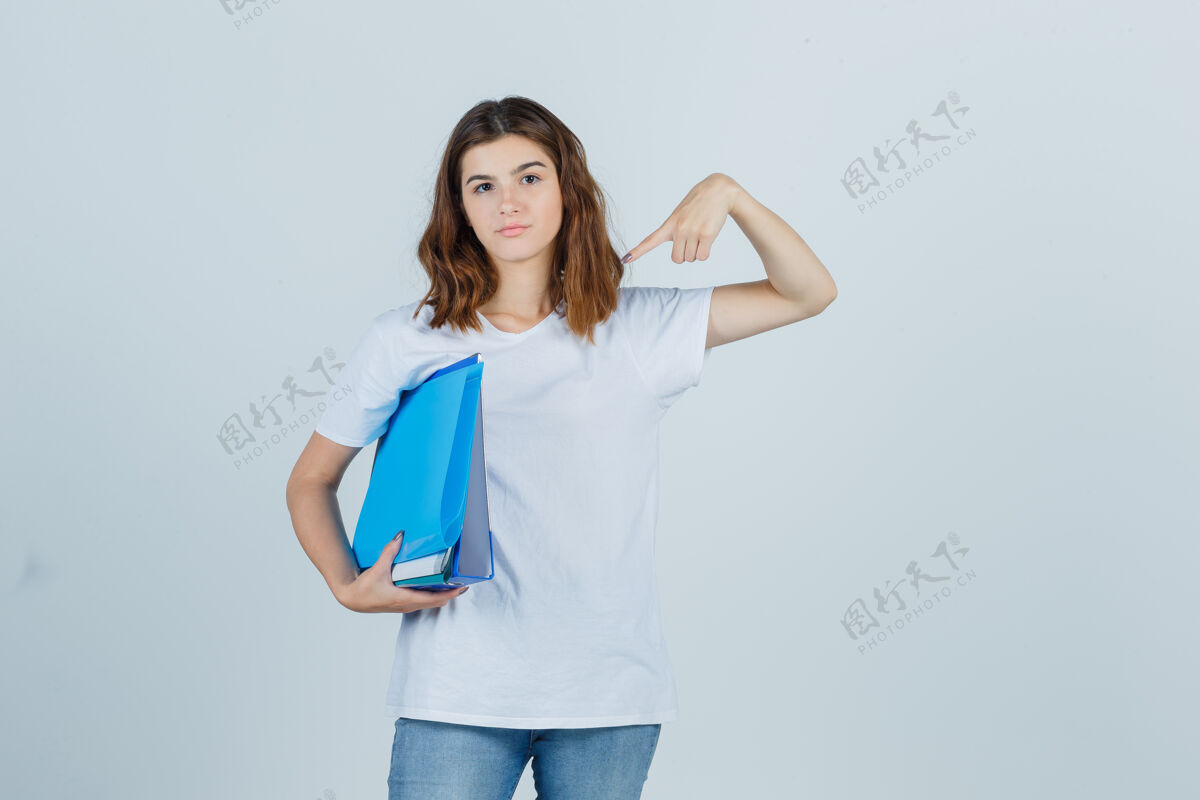 乐趣照片中的年轻女性指着文件夹 穿着白色t恤 牛仔裤 看上去自信满满年轻快乐头发
