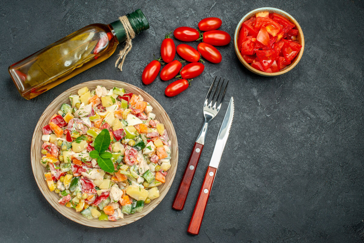午餐蔬菜沙拉的顶视图 深灰色背景上有番茄油瓶和餐具油西红柿黑胡椒