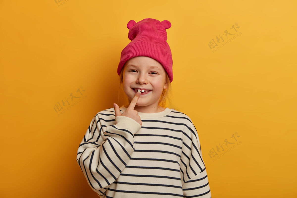脸漂亮小女孩儿的横拍表明她长了一颗新牙 关心牙齿 穿着时髦的衣服 表情滑稽 在室内咯咯笑 隔着亮黄色的墙指标模型欧洲