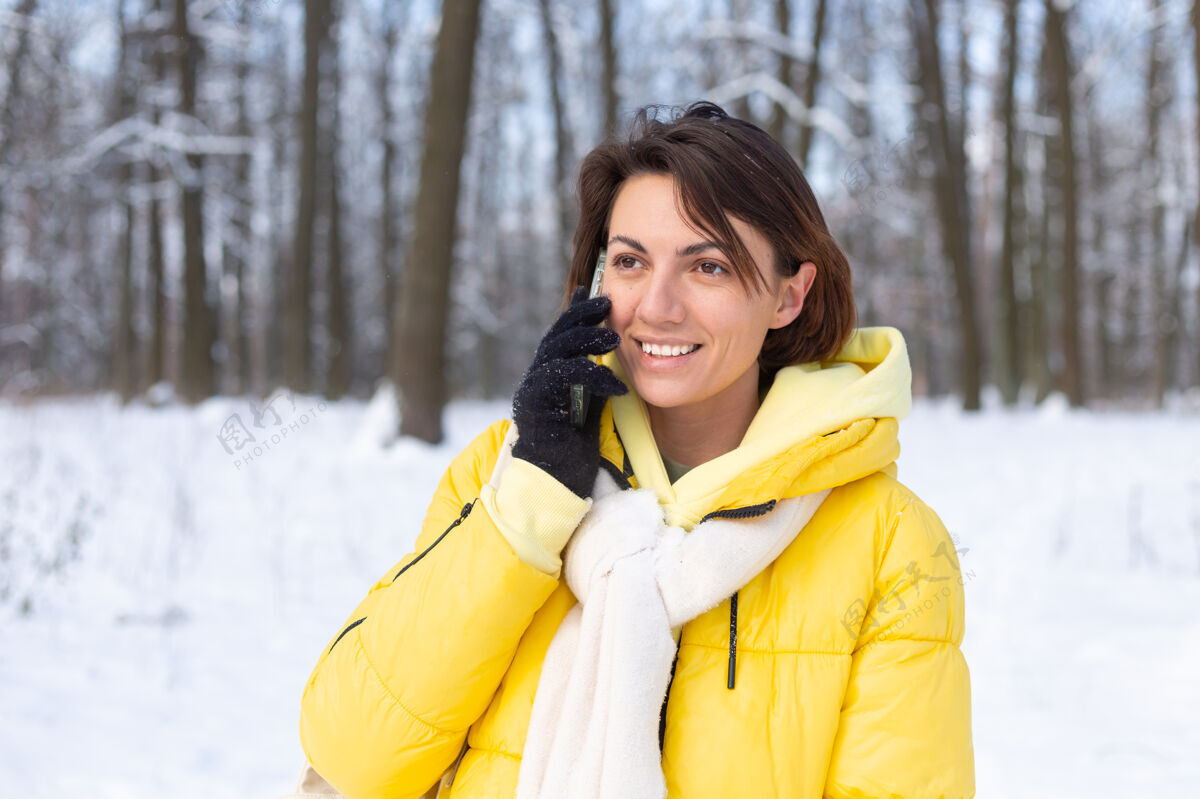 雪心情愉快的快乐女人漫步在雪域的冬日森林里 愉快地聊着电话 享受着公园里的户外时光站女性雪景