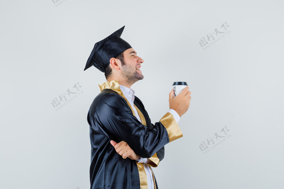 年轻年轻的男性拿着一杯咖啡 穿着研究生制服 看上去很高兴毕业男人男人
