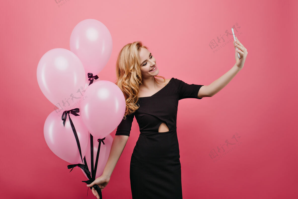快乐高兴的白人年轻女子用手机在她的生日自拍照片中的微笑浪漫的女士手持一堆聚会粉红气球肖像氦气球漂亮