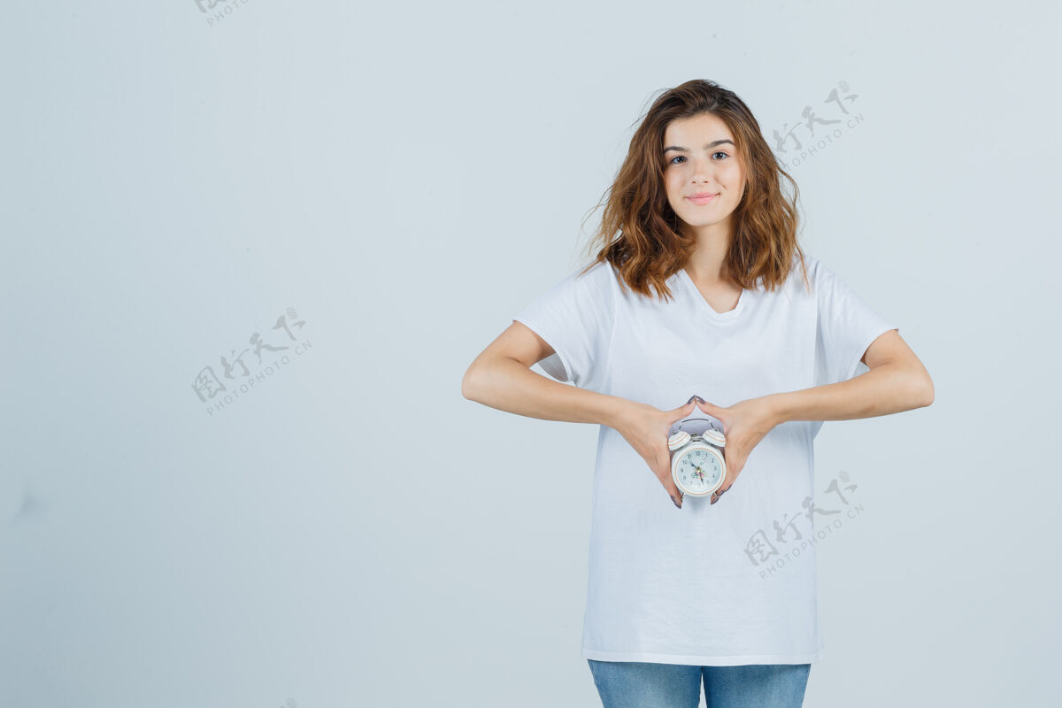 欢呼照片中的年轻女性手持闹钟 穿着白色t恤 牛仔裤 看上去很欢快闹钟皮肤女人