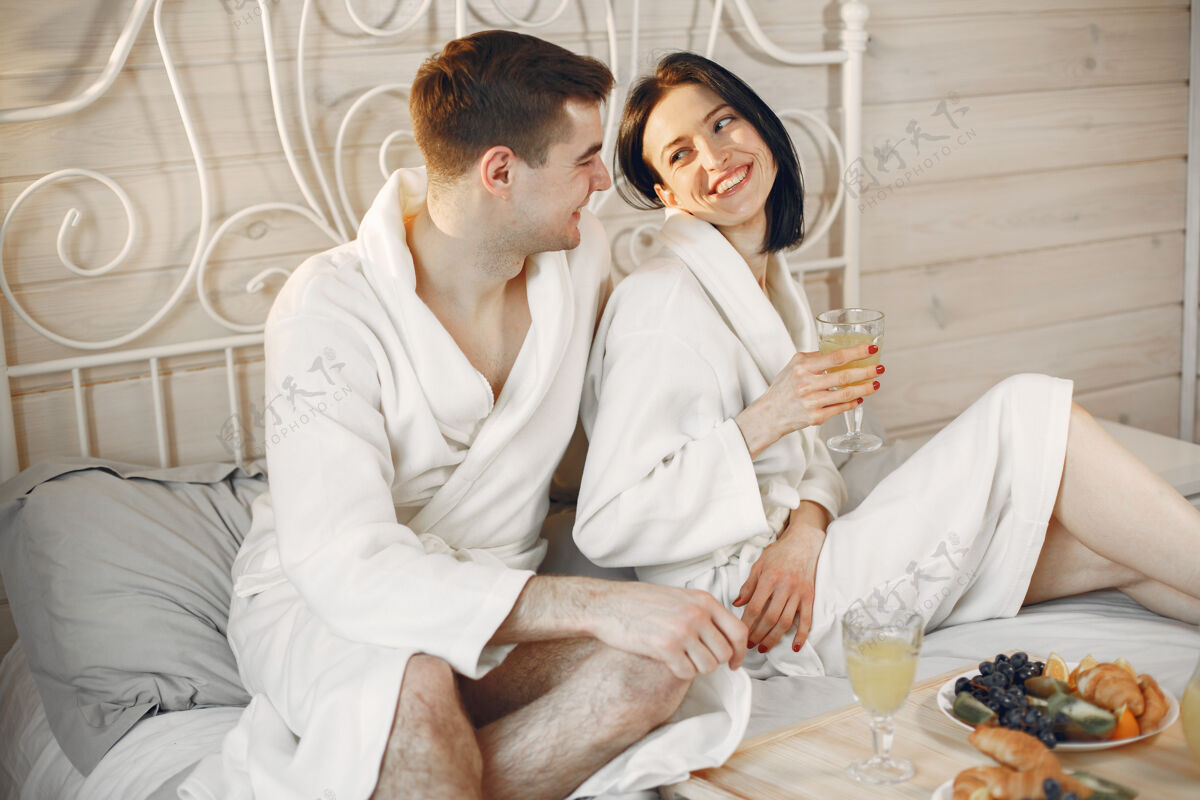 女人可爱的情侣穿着浴衣在卧室里吃早餐室内两个关系