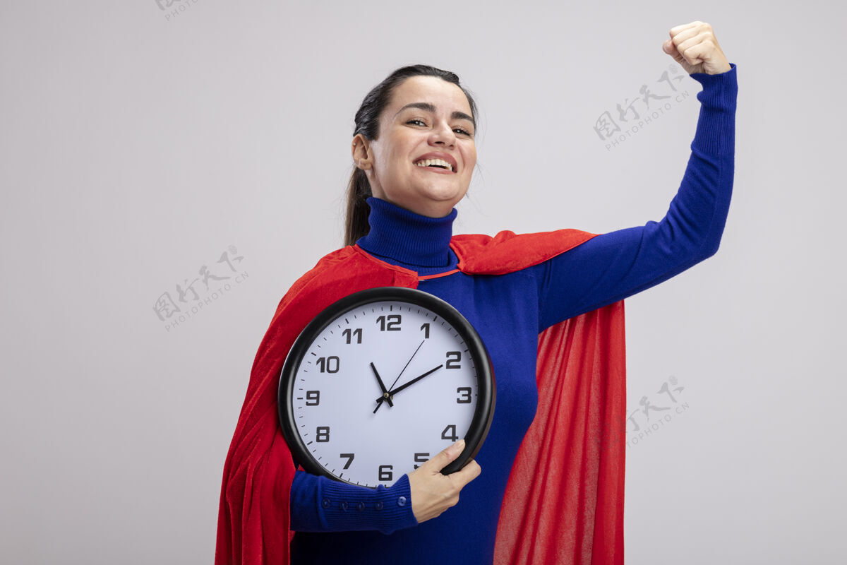 微笑微笑的年轻超级英雄女孩手持挂钟 在白色背景上显示出强烈的姿态握着女孩年轻