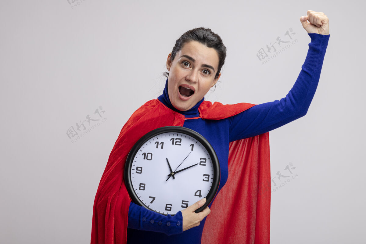 拿着快乐的年轻超级英雄女孩手持挂钟 在白色背景上显示“是”的手势墙壁超级英雄快乐