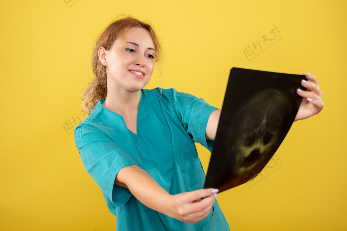 颜色正面图身穿医用衬衫的女医生拿着黄色桌子上的x光片彩色covid-19健康情感大流行病毒女医生医学女人