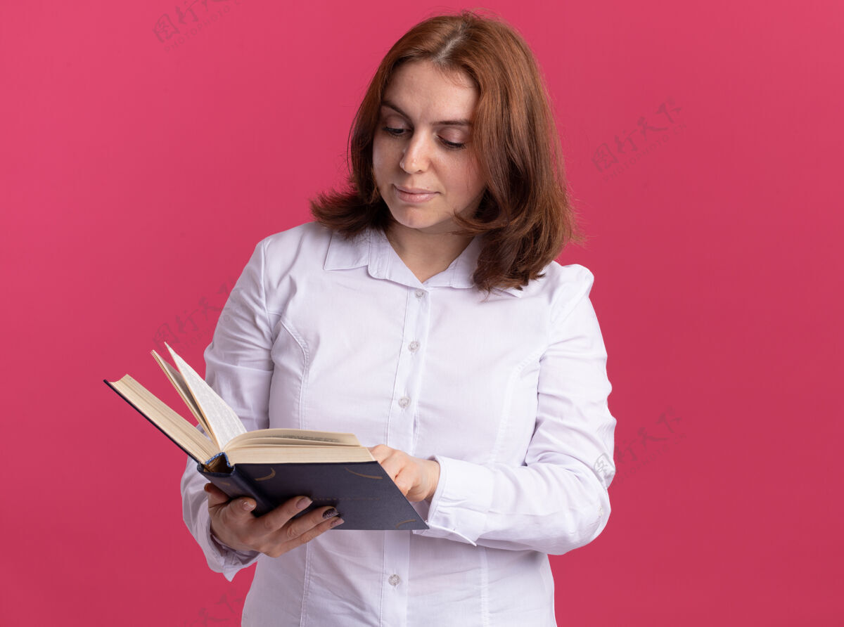 微笑身穿白衬衫的年轻女子面带微笑地拿着书站在粉红色的墙上年轻阅读抱着