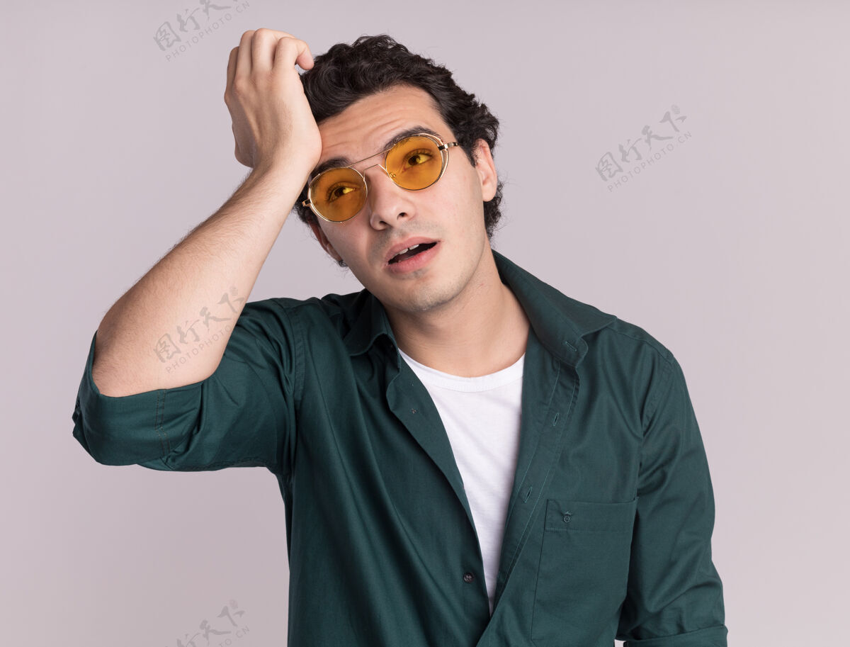 眼镜一个穿着绿衬衫戴着眼镜的年轻人站在白墙上 一边看一边又累又无聊靠边站戴着无聊
