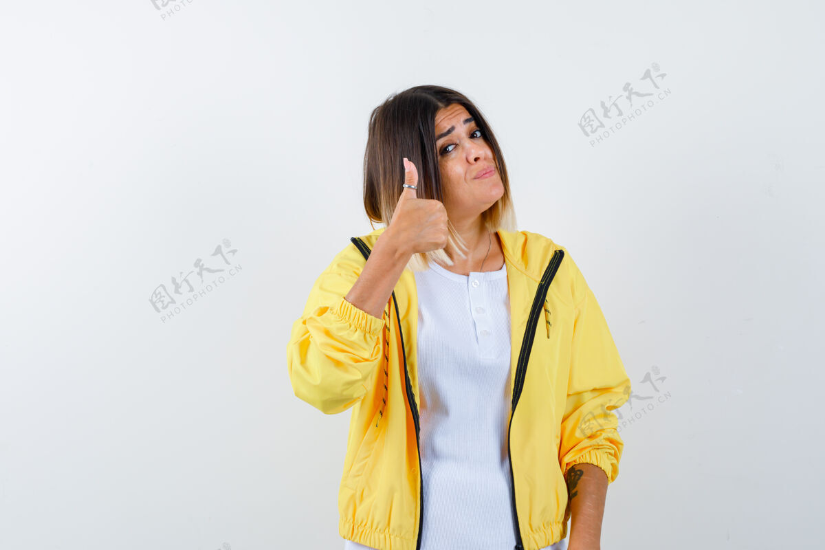 乐趣穿着白色t恤 黄色夹克的年轻女孩竖起大拇指 看上去很有吸引力 正面视图喜悦皮肤拇指
